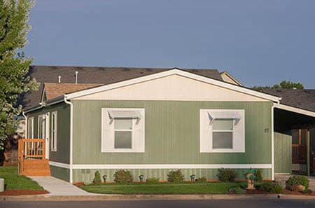 Nice and large olive colored manufactured home with carport and staircase.